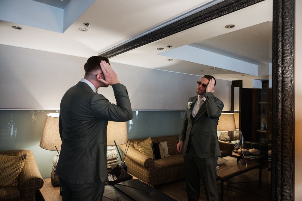 Two people in formal attire adjusting their ties in mirror reflection.