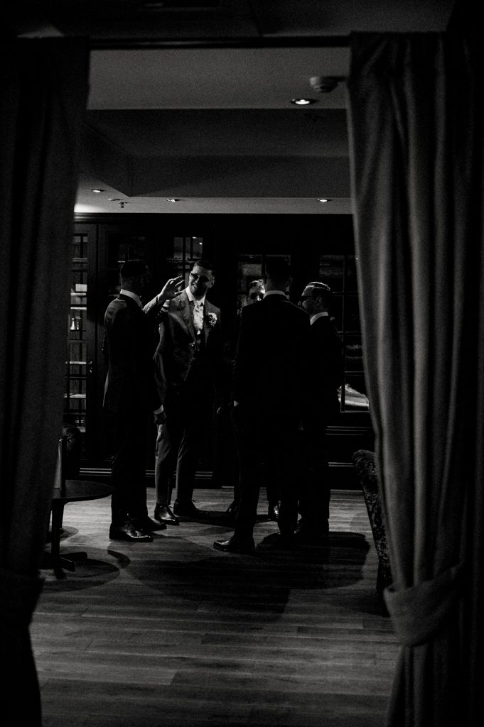 A dark silhouette of people gathered in conversation framed by curtains in a dimly lit venue.