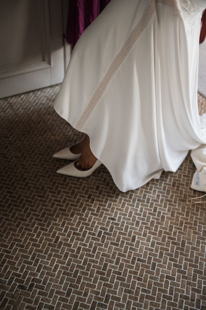 White wedding dress hem and elegant white bridal shoes peek out against a geometric patterned carpet.