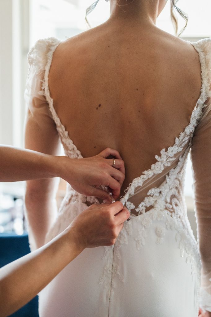 Close-up of hands fastening buttons on a white lace wedding dress.