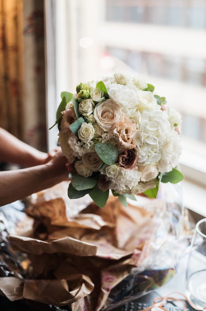 A delicate bridal bouquet featuring white hydrangeas, blush roses and greenery sits on brown paper wrapping.