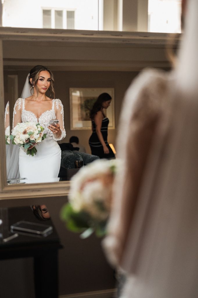 Wedding dress reflection in mirror with bouquet of white flowers.