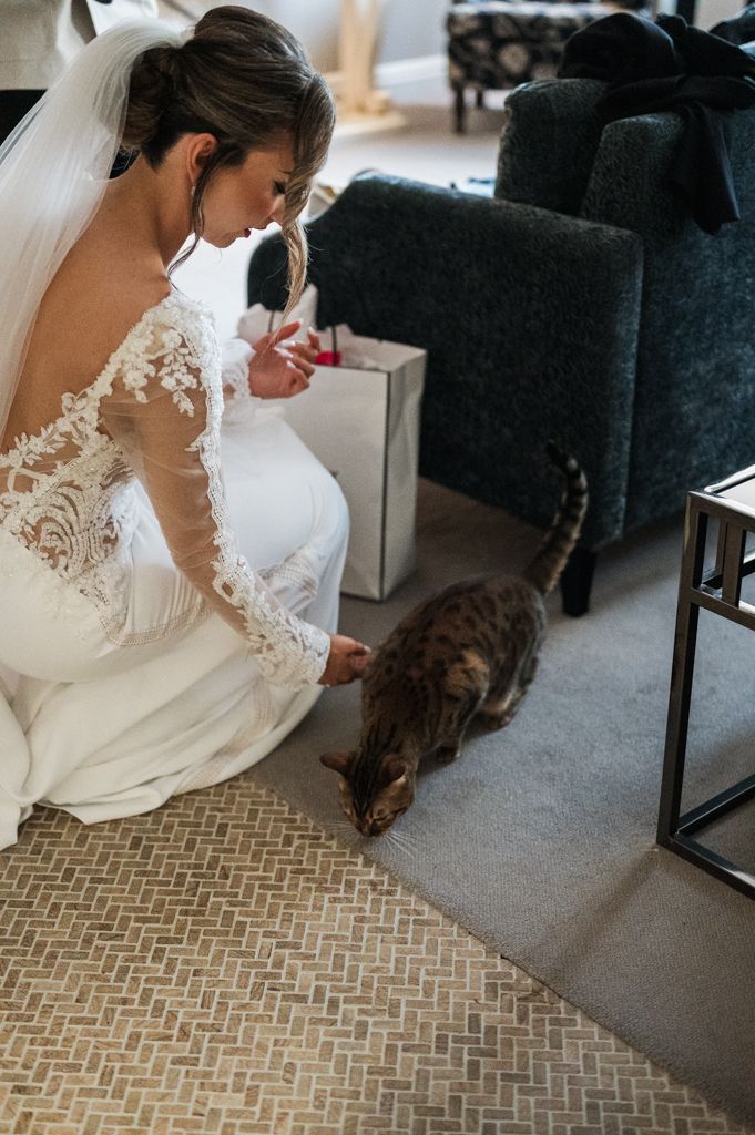 Bride in lace wedding dress bending down to pet a small dark-colored dog.
