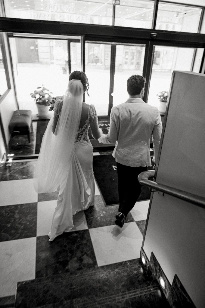Black and white photo of couple descending stairs in wedding attire.