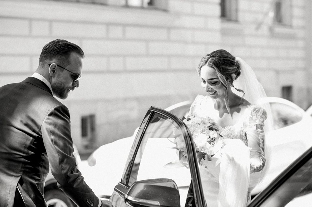 A joyful wedding moment captured in black and white as a couple enters their car.