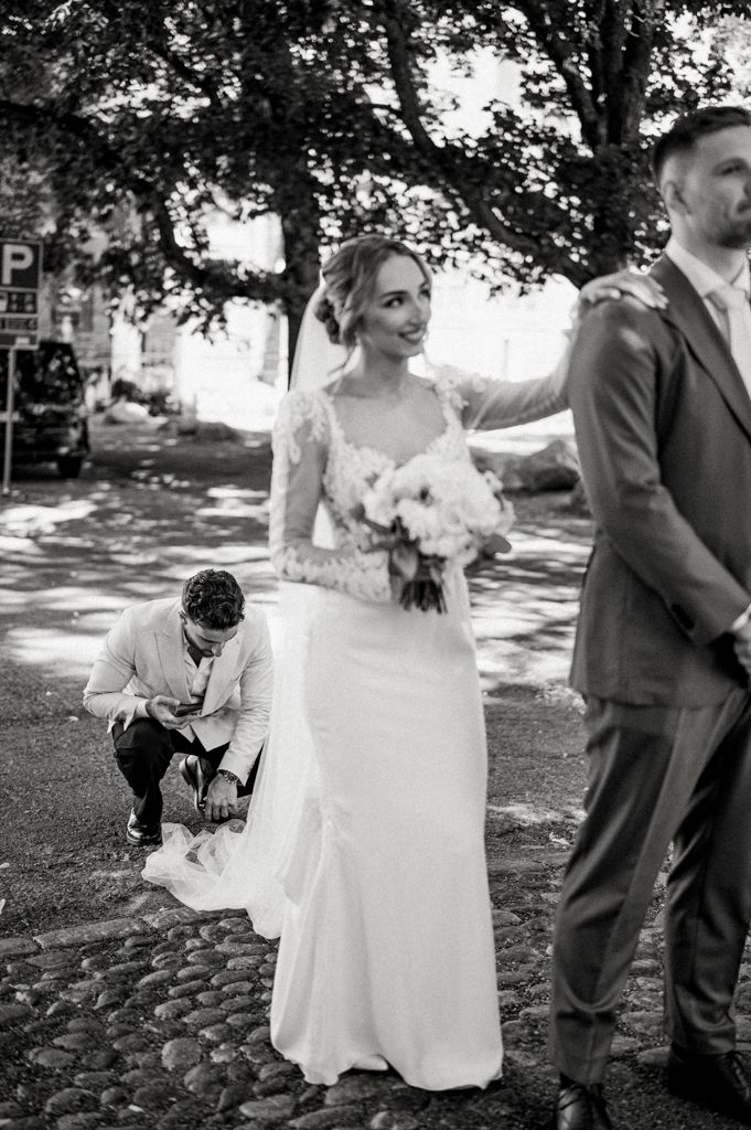 Candid black and white wedding photo with figures outdoors on a cobblestone path under trees.