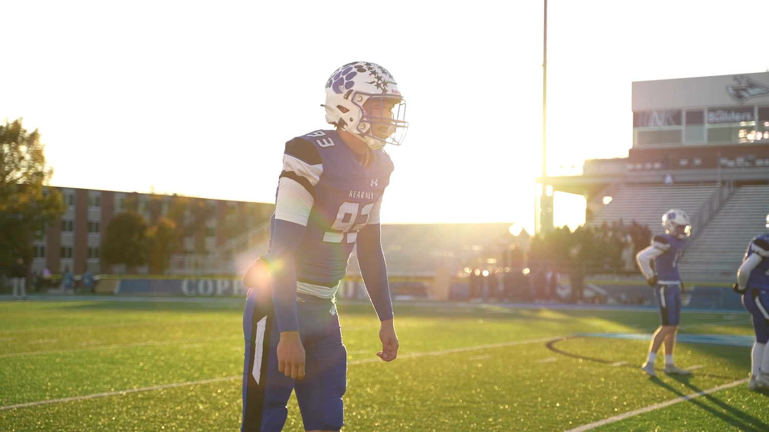 Football player stands on field during golden hour sunset practice.