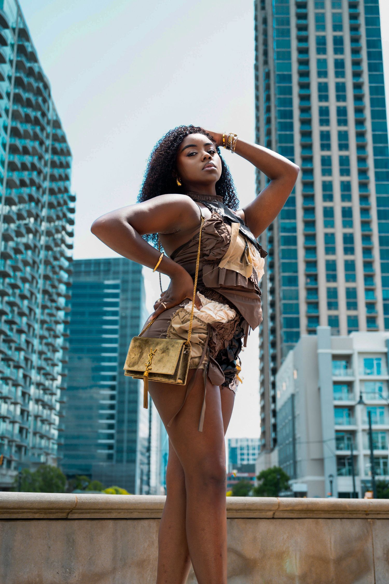 A model poses stylishly in front of modern high-rise buildings wearing urban fashion and accessories.
