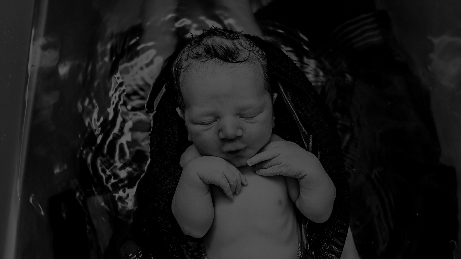 An intimate black and white image of a mom holding her baby in the bathtub shortly after birth