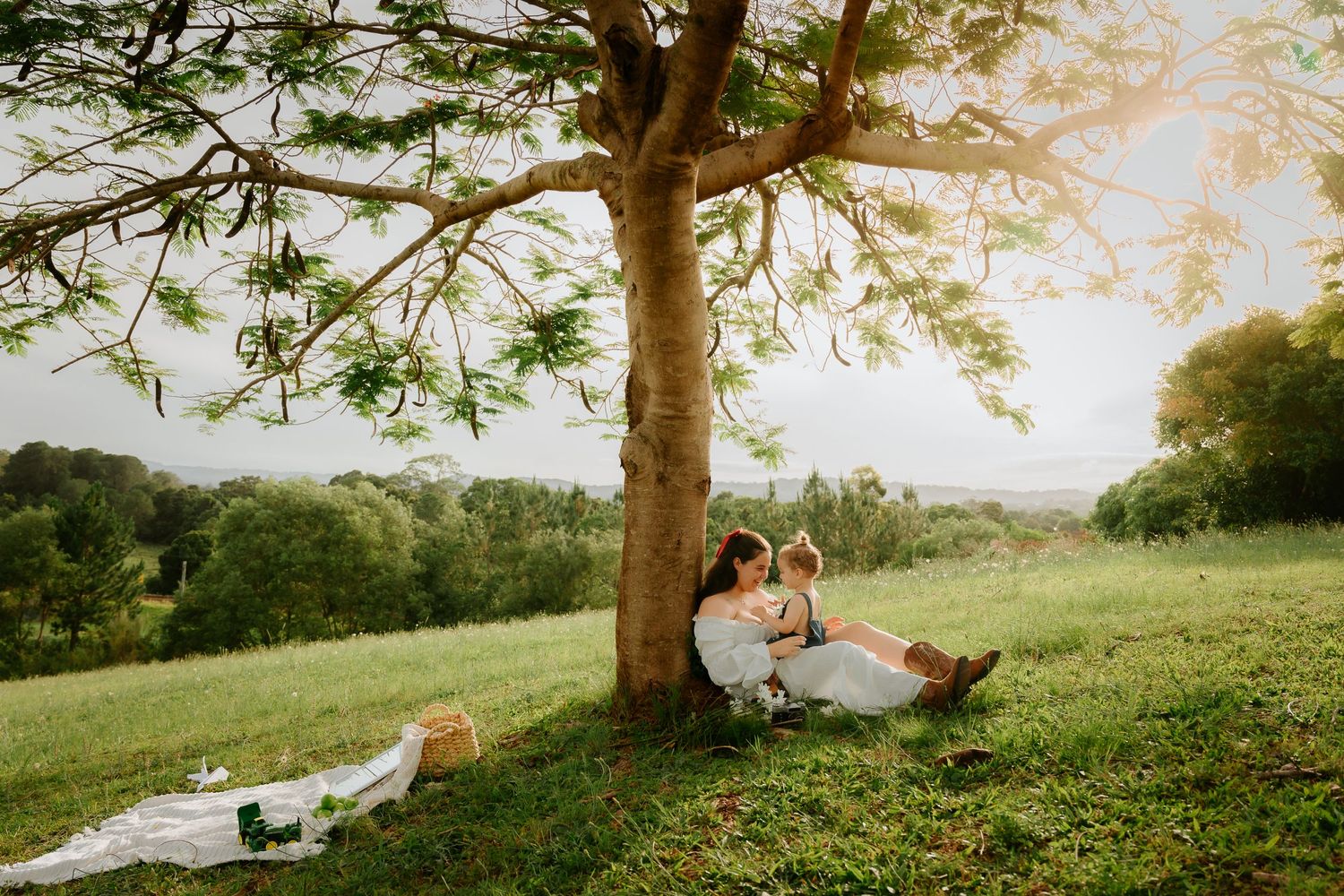 Couple having picnic under large tree in sunny meadow.