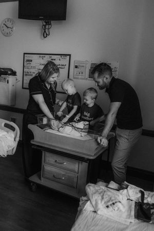 Medical professionals attend to a young child on an exam table in a black and white hospital setting.
