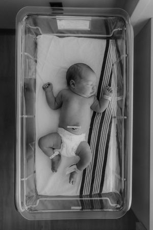 Black and white overhead view of four sequential medical bassinets containing sleeping infants in hospital setting.