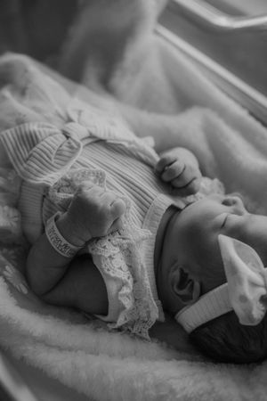 A sleeping newborn baby wrapped in white blankets and linens rests in a monochrome black and white photograph series.