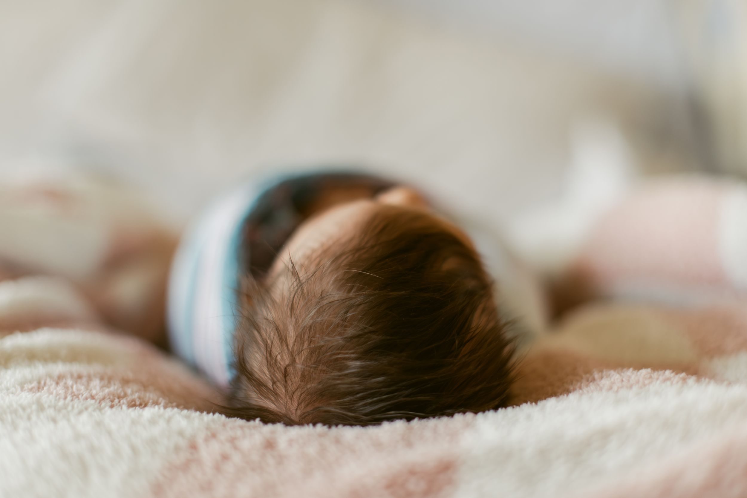 A small baby lies sleeping peacefully in a white bed with soft bedding and gentle natural lighting.