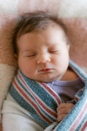 Peaceful sleeping baby wrapped in a striped blue and pink blanket.