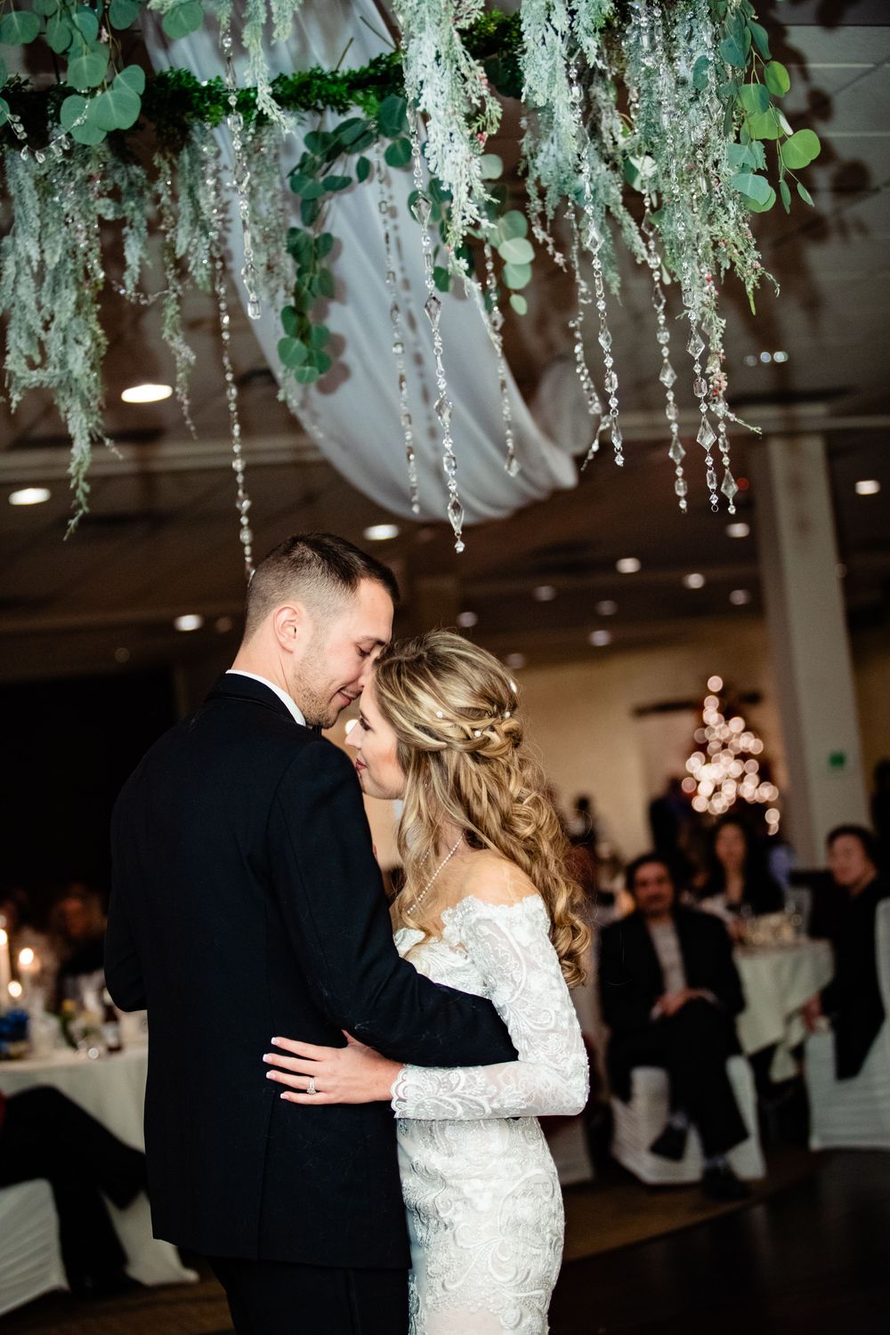 Bride and groom share their first dance under hanging greenery and crystal decor at elegant wedding reception.