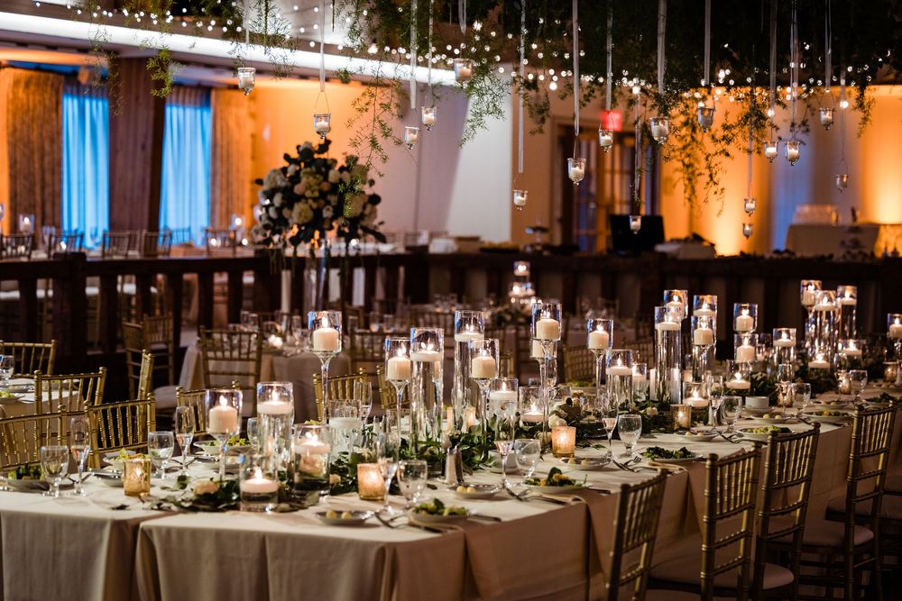 Elegant wedding reception with gold Chiavari chairs, candlelit tables, greenery centerpieces, and string lights overhead.