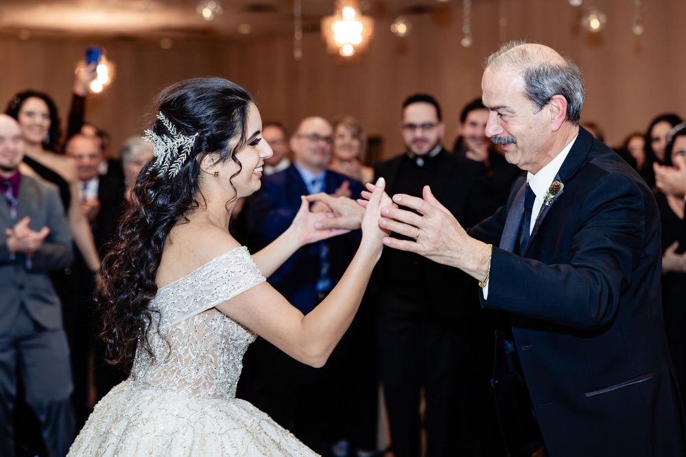 Young woman in ball gown dances with older man at elegant quinceañera celebration while guests applaud.