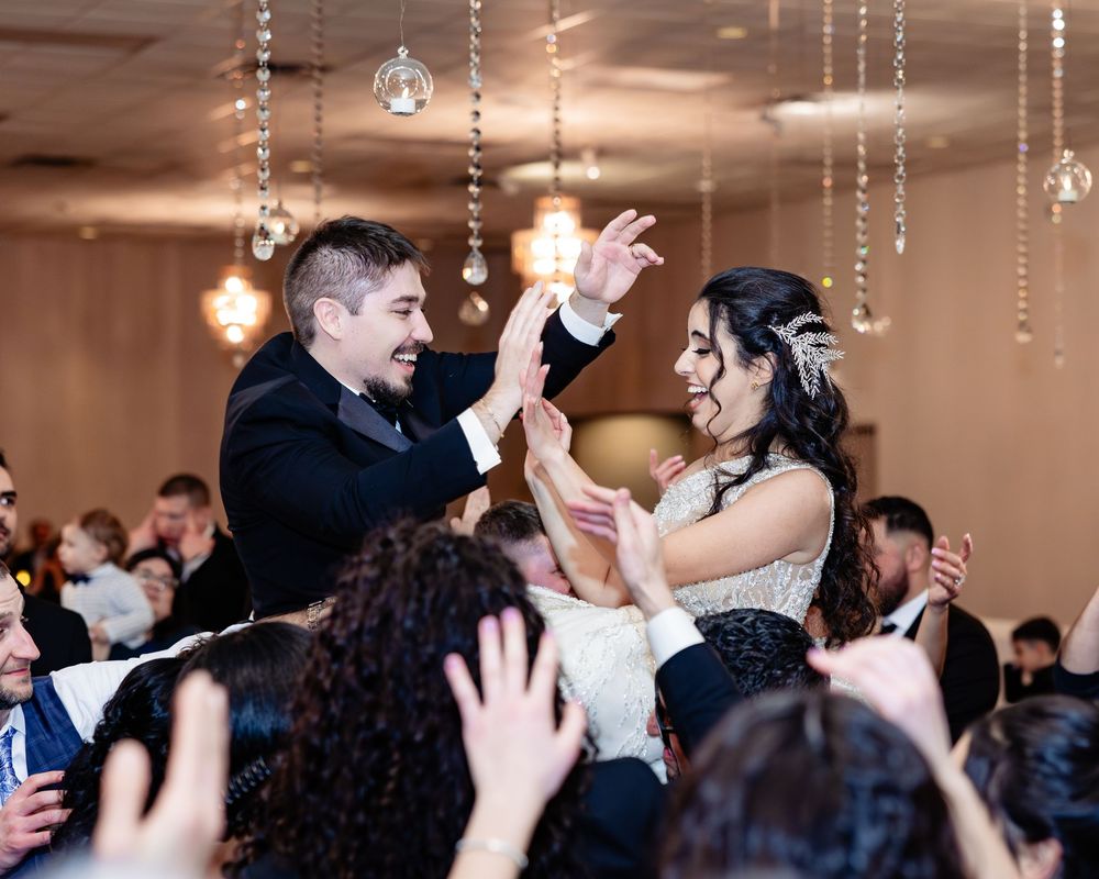 Bride and groom share joyful first dance at elegant wedding reception with crystal chandelier decorations.