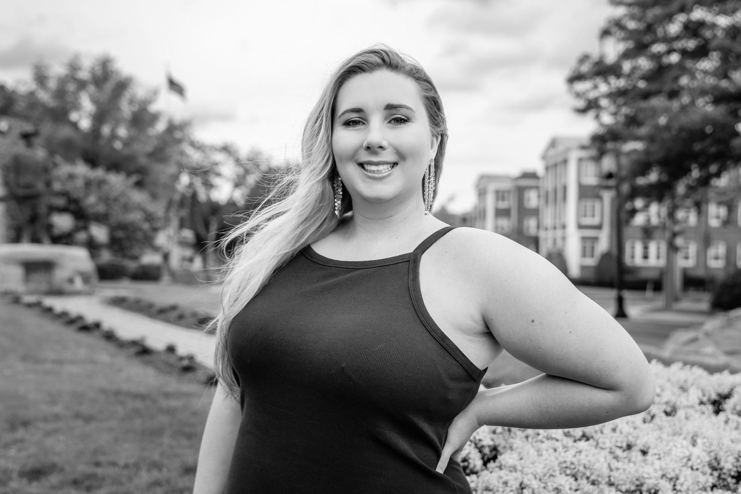 Black and white portrait of a woman in a sleeveless top posing outdoors with a natural smile.