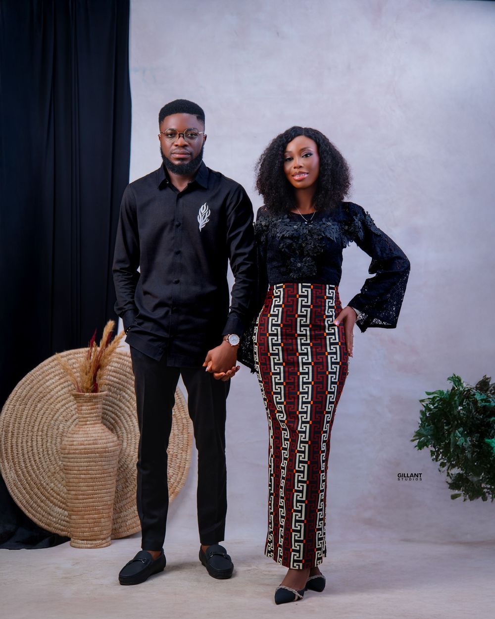 Stylish couple poses in traditional African attire with decorative fan against neutral background.