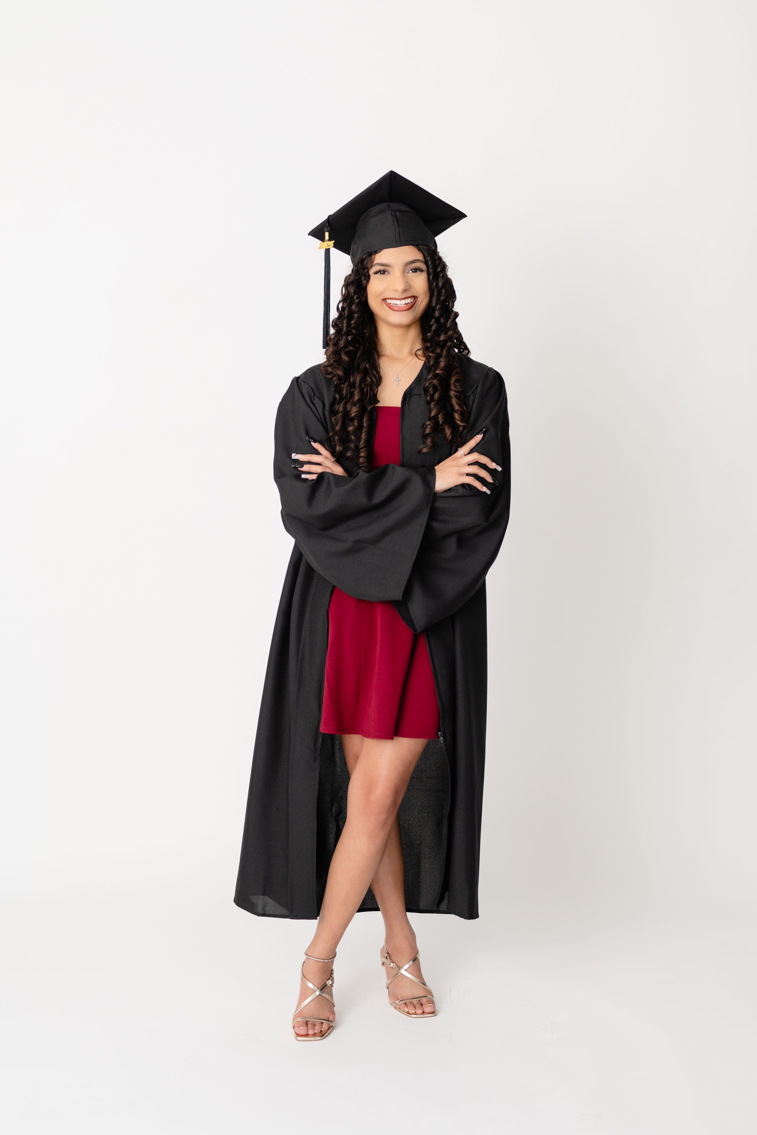 Graduate wearing traditional black cap and gown with red dress underneath poses confidently against white background.