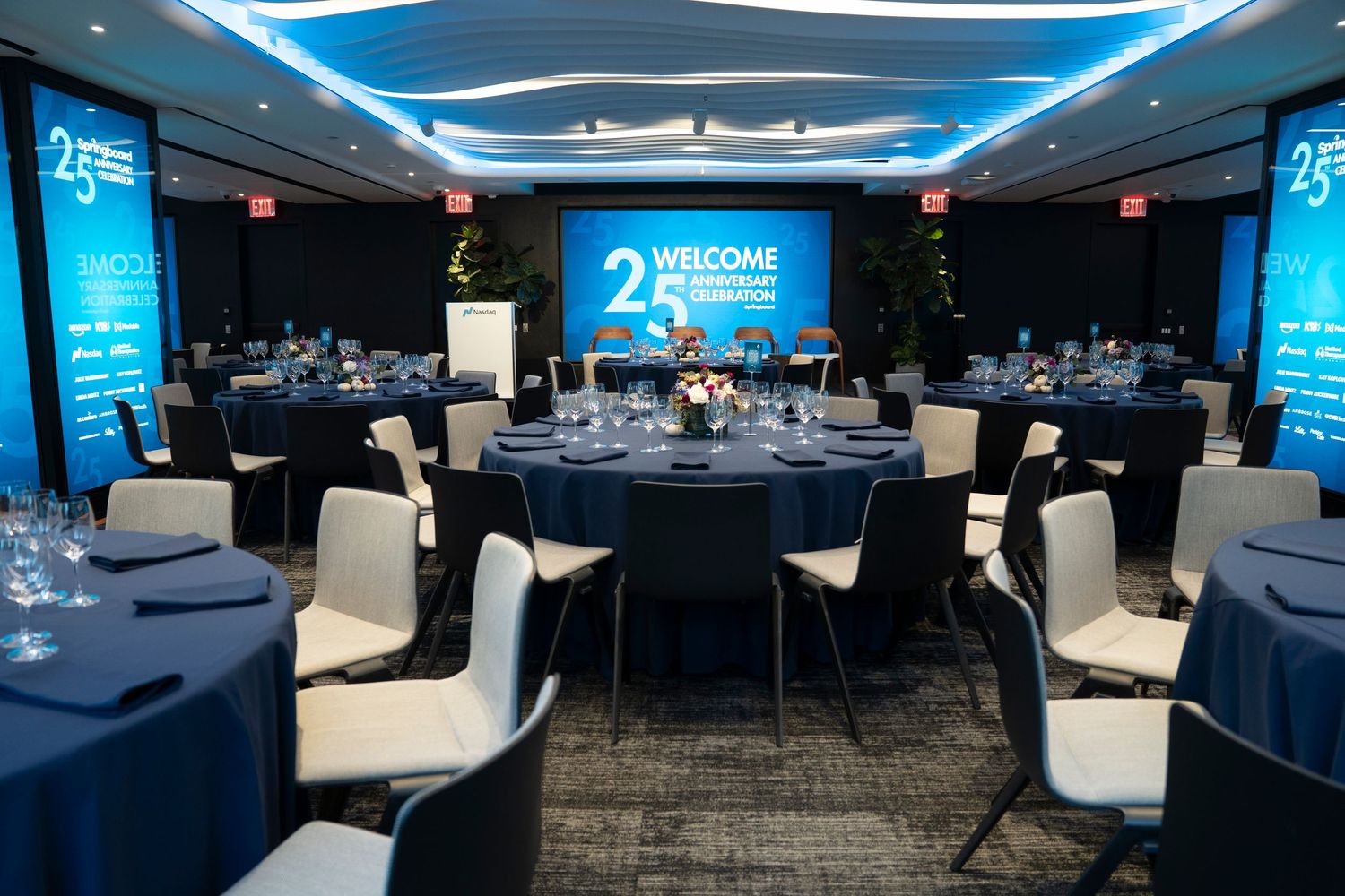 Corporate event space with blue LED lighting, white chairs, and dark tables set up for a conference or meeting.