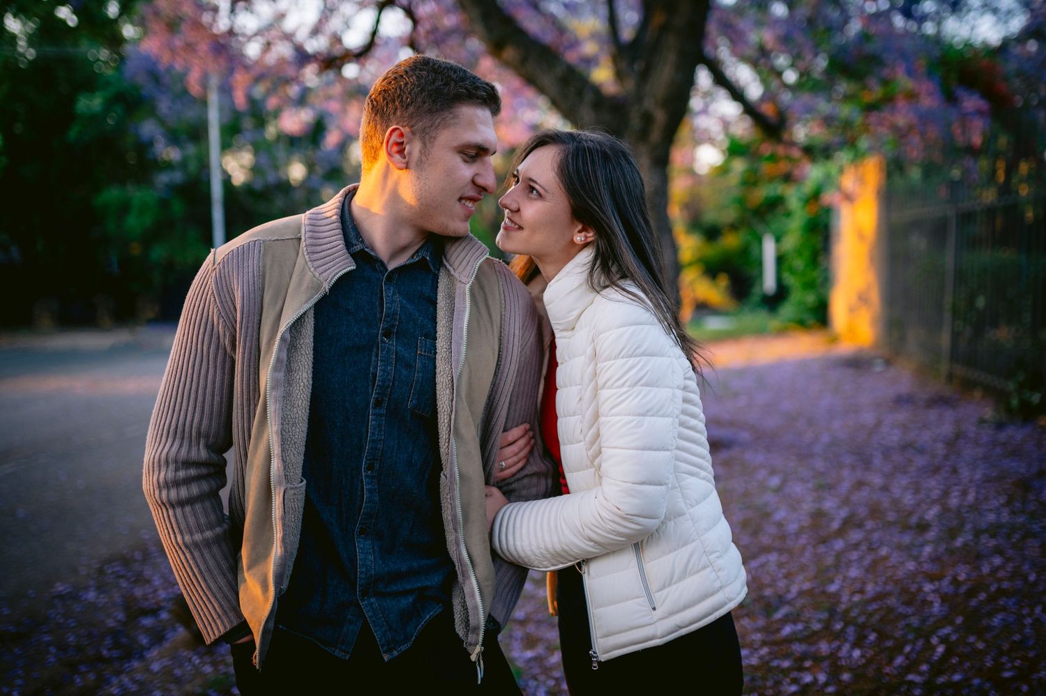 A romantic couple shares tender moments together in a garden filled with blooming purple jacaranda trees.