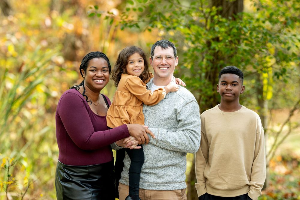 Happy blended family of four posing together in a colorful autumn outdoor setting.