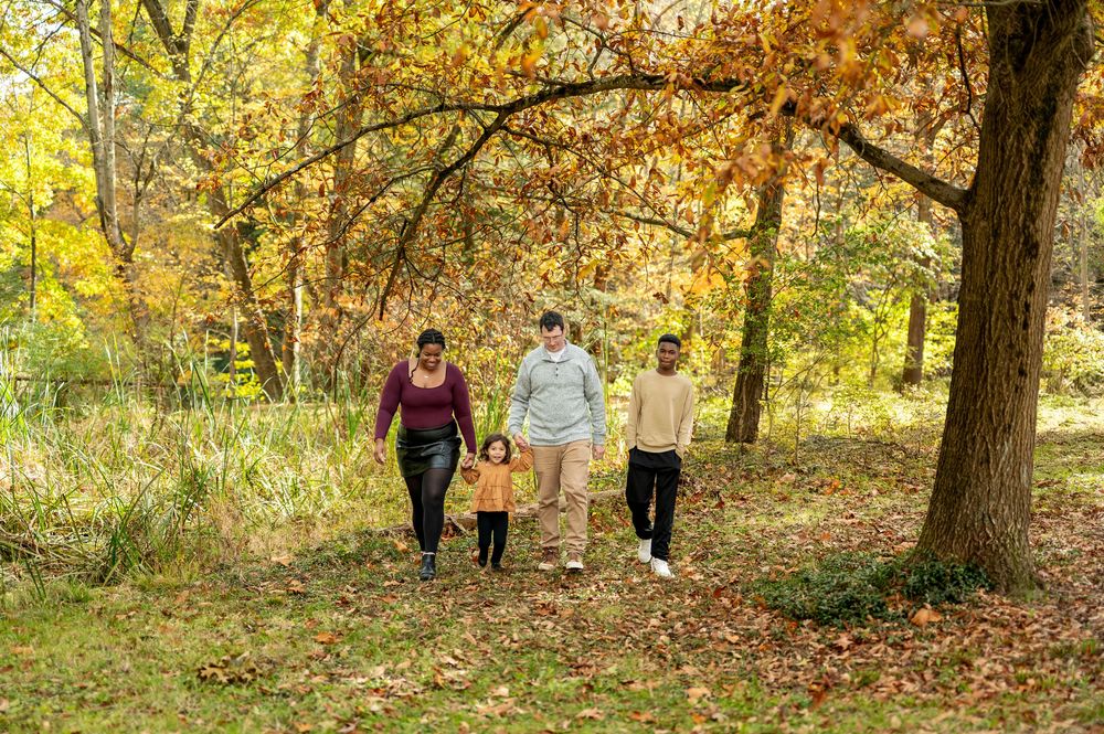 Family of four strolling together through sunlit autumn park with golden and orange foliage.