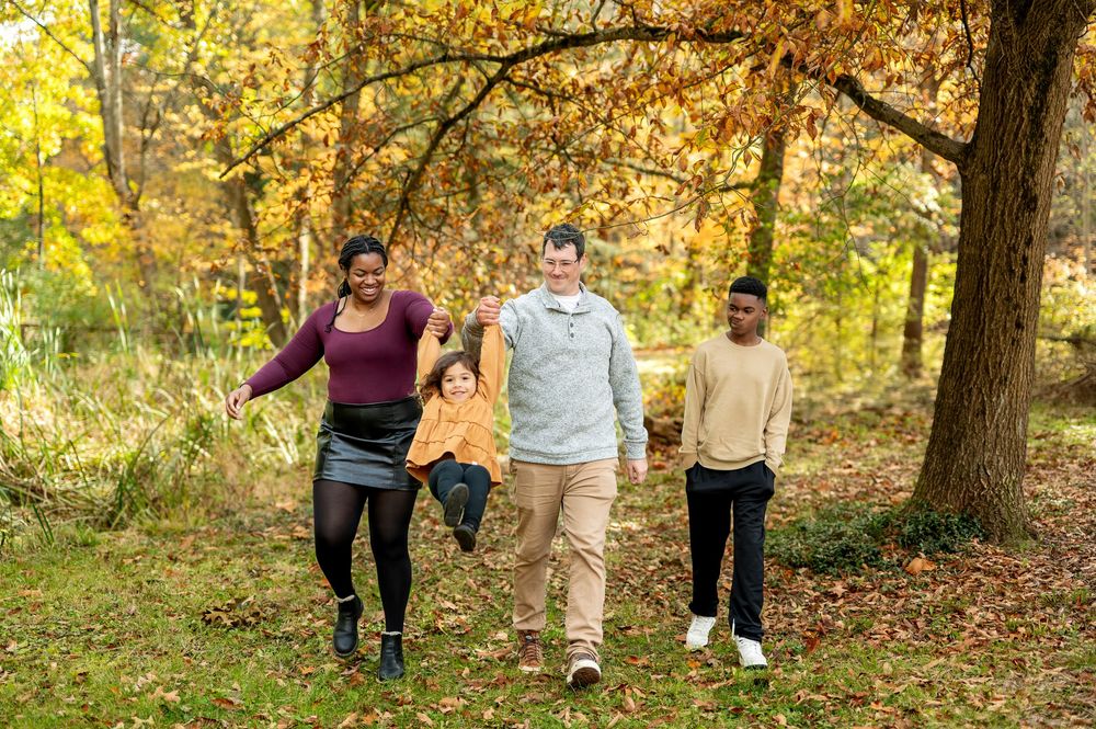 Happy family of four walking and laughing together through golden fall foliage in park.