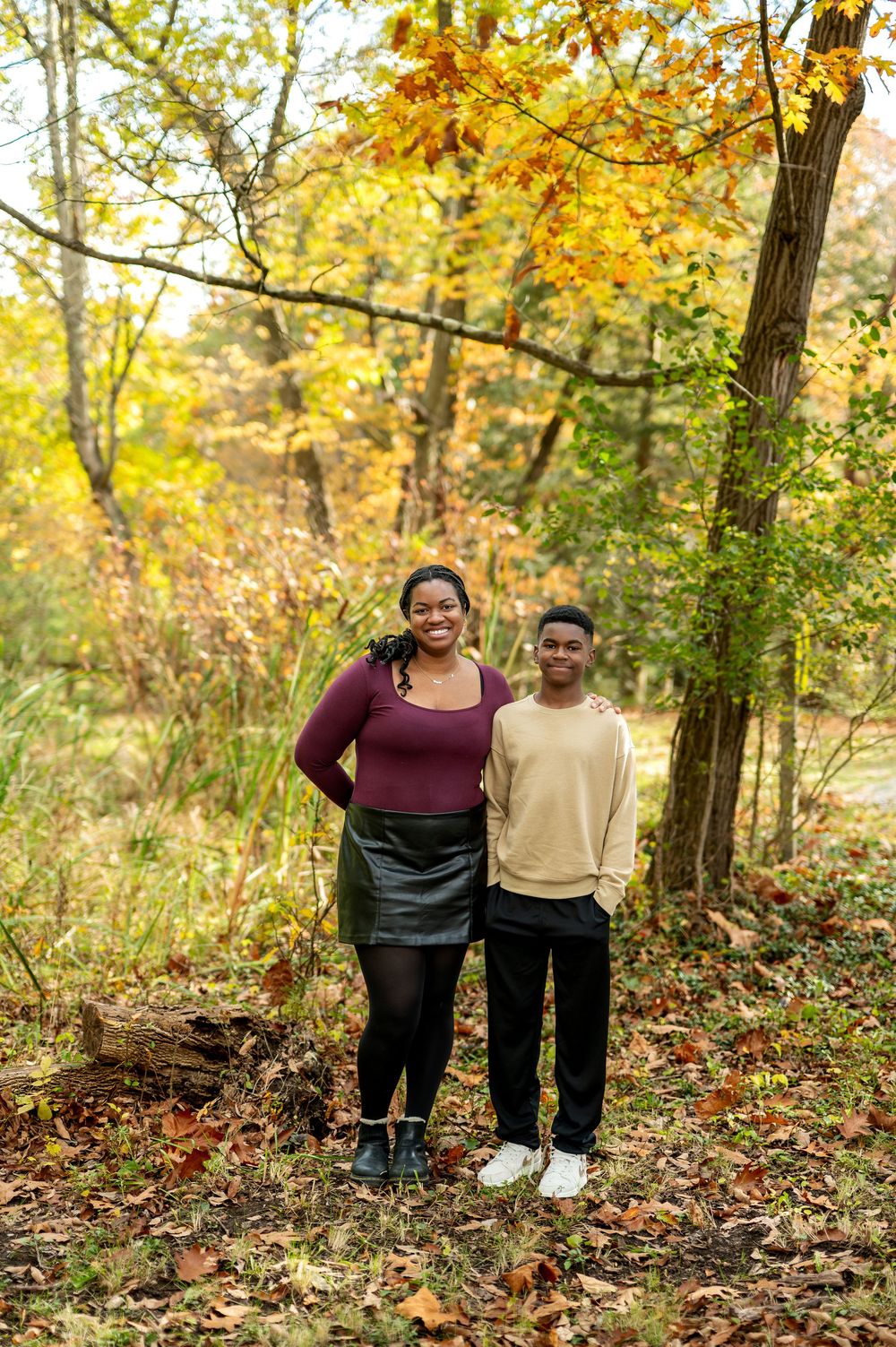 Smiling Black mother and teenage son standing together in a colorful autumn forest setting.