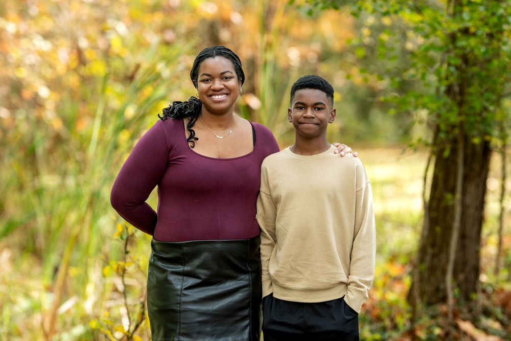 Happy Black mother and teenage son smiling together outdoors in a golden autumn park.