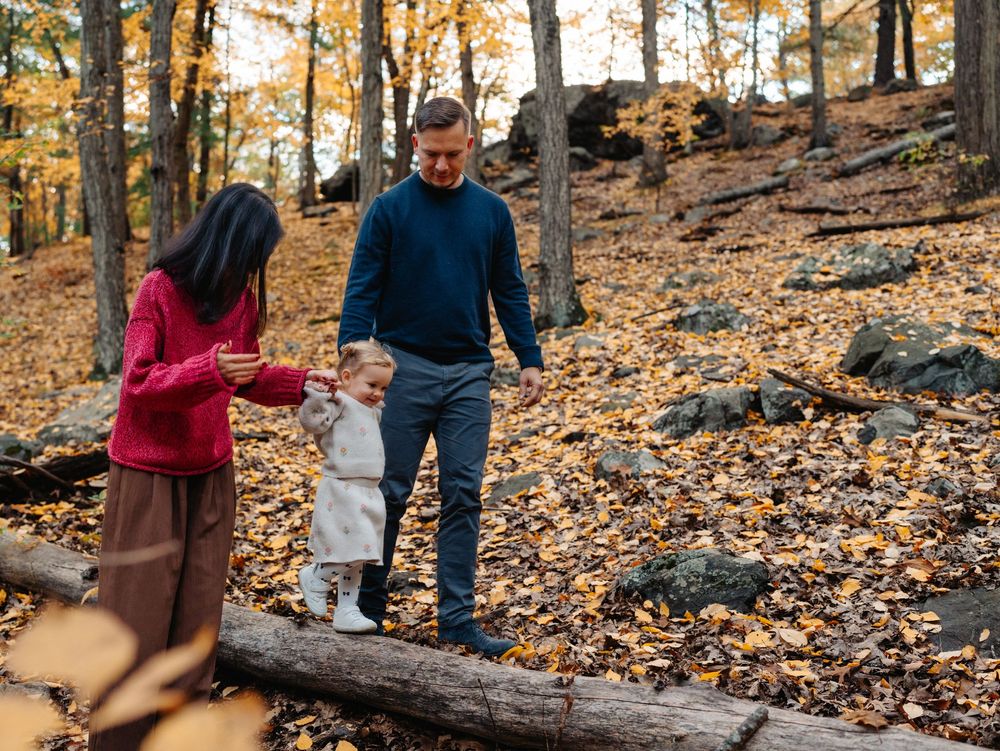 Family walks together through fallen leaves on forest trail during golden autumn afternoon, Menotomy-rocks-park in Arlington, MA.