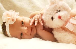 A baby lying on soft white fabric smiles while holding a plush toy.