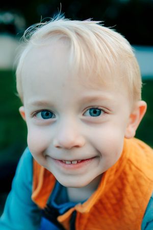 Close up portrait of a toddler in an orange vest smiling with bright blue eyes.