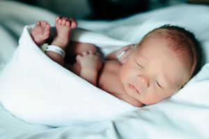 Peaceful sleeping newborn baby wrapped in soft white blankets rests with tiny hands visible.
