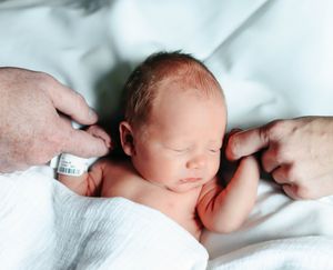A sleeping newborn baby rests peacefully on soft white bedding in a tender close-up portrait.