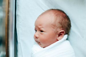 A newborn baby sleeps peacefully in a white blanket against a light blue background.
