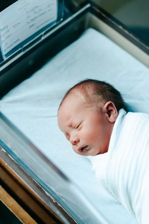 Newborn baby sleeping peacefully in white hospital bassinet viewed from different angles.
