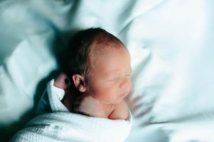 A newborn baby sleeps peacefully on white bedding in a soft, dreamy lighting setup.