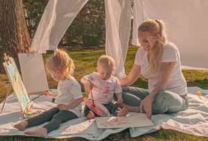 Family enjoying outdoor reading time together on a white blanket in dappled sunlight.