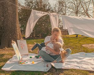 A cozy outdoor picnic setup with white linens and blankets spread on grass during sunset.