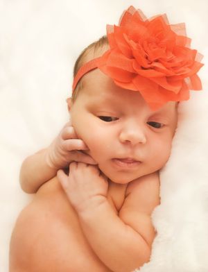 Baby wearing a bright coral flower headband lying on white fabric.