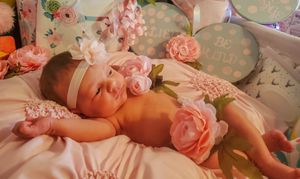 Sleeping newborn baby wrapped in pink blanket surrounded by soft pink roses and floral decor.
