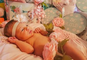 Delicate pink roses and floral decorations create a soft, romantic newborn photography setting.