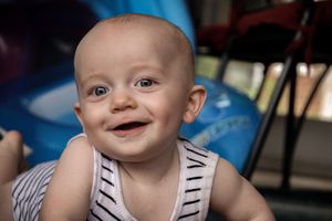 Baby wearing a striped outfit smiles brightly against a blue background.