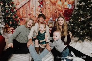 Family group poses together in front of Christmas decorations and trees during holiday photo session.