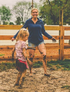 People playing and splashing in a muddy outdoor enclosure surrounded by wooden fencing.