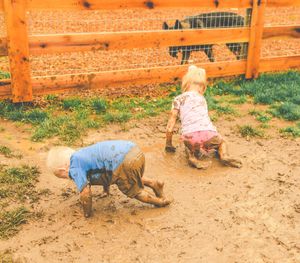 A child plays joyfully in the dirt near a wooden fence on a sunny day.